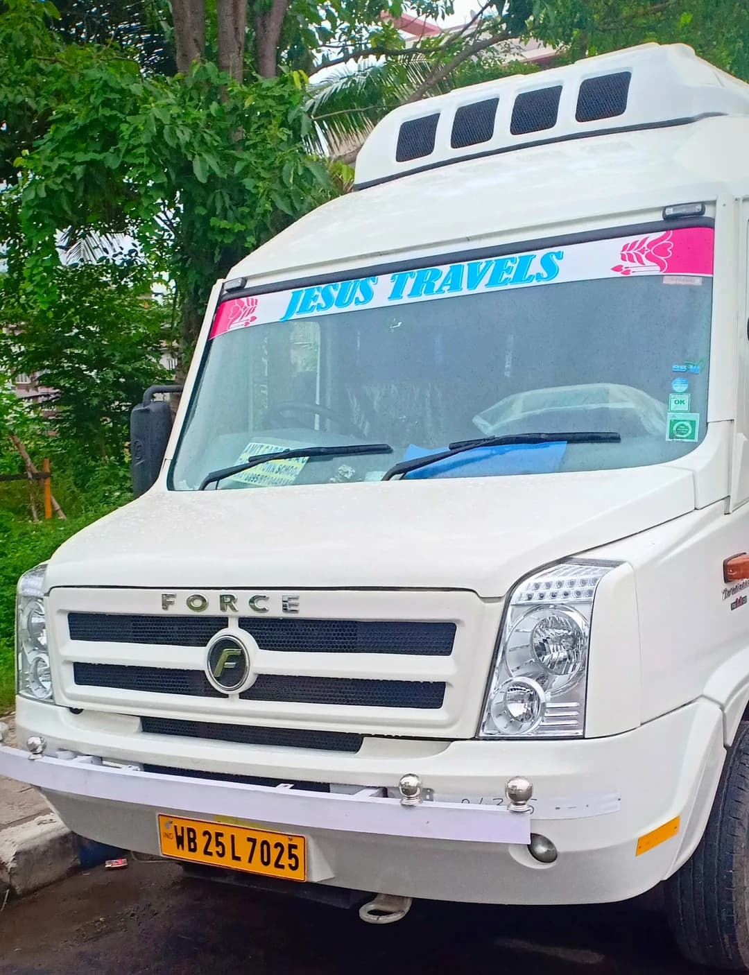 A Jesus Travels passenger vehicle parked outdoors beneath trees